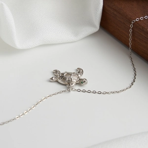 Detail of S925 sterling silver sea turtle necklace with green stone eye on white silk