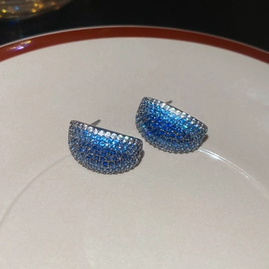 Macro shot of silver C-shaped earrings with blue and white gradient zircon on ceramic tray