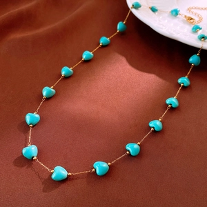 Detail of turquoise heart beads on a fine gold-tone chain necklace over brown silk