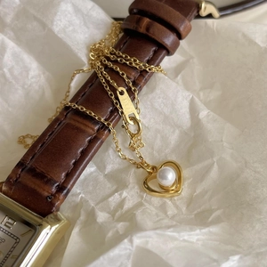 Detail of a gold heart pendant with white pearl on a vintage brown leather watch strap