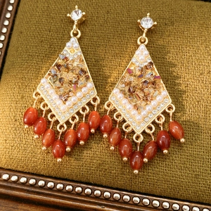 Primer plano de pendientes vintage en forma de rombo con perlas y borlas naranjas