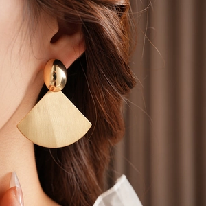 Close-up of golden oval stud and fan-shaped earring with brushed metal texture