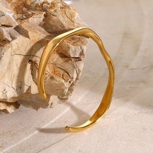 Close-up of golden wavy cuff bracelet displayed on a natural rock with mirror finish