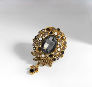 Detailed view of vintage gold floral brooch with grey rhinestones and glass pendant