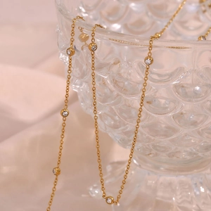 Macro shot of gold necklace with round zircon charms hanging on a textured glass rim