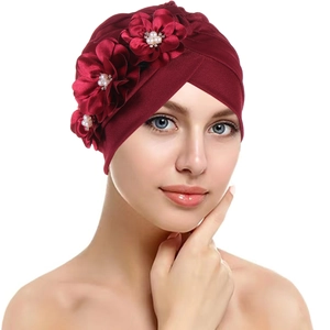 Detail of burgundy turban cap featuring three silk flowers with central pearl accents