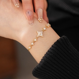 Detail of a gold star bracelet with white zircons on a model's wrist with black sleeve