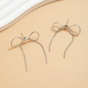 Detailed view of silver bow earrings crafted from delicate metal snake chains on warm background