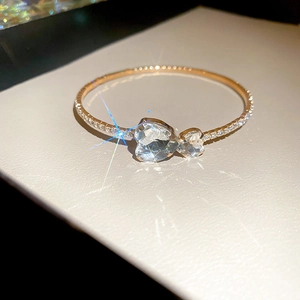Close-up of gold bangle featuring pave diamonds and two interlocking heart-shaped zircons