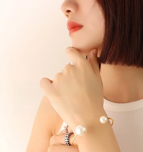 Close-up of elegant gold plated bangle with faux pearls and matching enamel rings on model