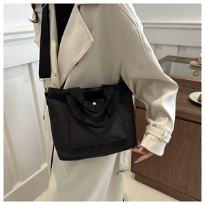 Detalle de un bolso tote grande de nailon negro llevado por modelo con abrigo beige