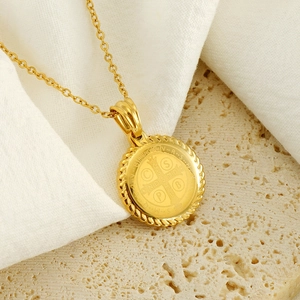 Gros plan du collier médaille Saint-Benoît en or sur travertin beige et tissu blanc