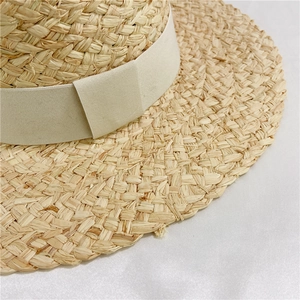 Detail of hand-woven raffia straw texture and wide beige fabric ribbon on sun hat