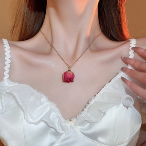 Detail of elegant gold chain necklace featuring a real dried dark red rose flower pendant