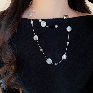 Detail of double-layer necklace with white pearls and mother-of-pearl on black knitwear