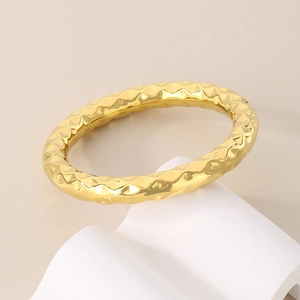Minimalist gold stainless steel bangle with a hammered geometric texture on white pedestal