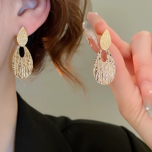 Detail view of gold teardrop earrings with textured metal finish on a model's ear