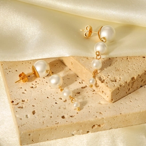 Macro view of long pearl earrings with gold studs displayed on soft silk fabric