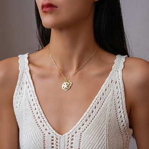 Nahaufnahme einer goldenen Halskette mit rundem Relief-Blumenanhänger am Hals des Models