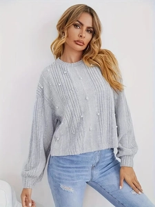Gros plan sur un pull en maille grise orné de perles blanches avec texture côtelée