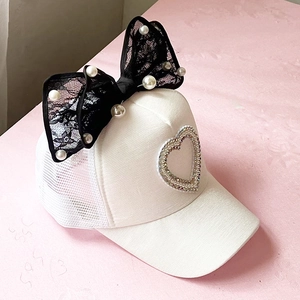 Detailed view of white mesh baseball cap featuring a large black lace bow and pearls