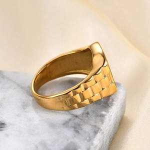 Detail showing golden signet ring with watch-band texture on marble base