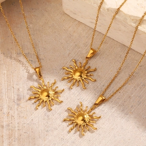 Trois colliers avec pendentif soleil en acier plaqué or 18K sur une surface en pierre