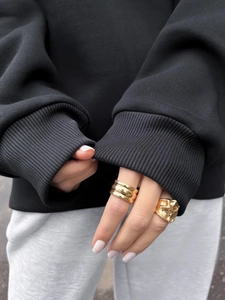 Close-up of chunky gold rings set on black hoodie sleeve highlighting metallic texture