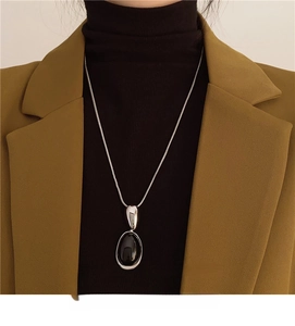 Detail of silver snake chain with oval black resin pendant on professional office attire
