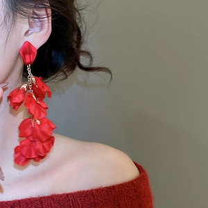 Macro detail of red fabric flower earrings with elegant long tassels and gold chain accents