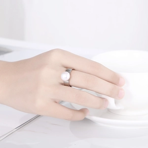 Detail of wide silver ring with large round pearl on a model's hand holding a cup