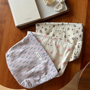 Three-piece set of floral cotton cosmetic bags in lavender and cream on wooden table