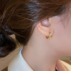 Gros plan sur une boucle d'oreille dorée en forme de U portée par un mannequin