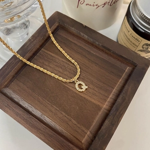Détail macro du pendentif lettre Q dorée avec cristaux blancs sur une chaîne à mailles torsadées