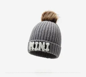Detail of grey ribbed knit beanie with brown faux fur pom-pom and white MINI patch