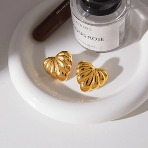Close-up of 18k gold plated chunky heart earrings with shell texture on ceramic plate