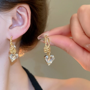 Close-up of heart-shaped crystal earrings with golden twisted metal detailing