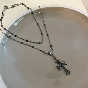 Détail macro d'un collier à double épaisseur avec pendentif croix et pierres précieuses noires