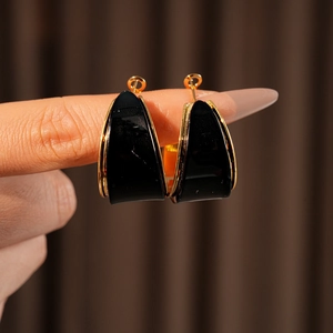 Macro shot of gold-plated resin hoop earrings held between fingers showing sleek finish