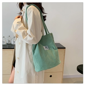 Detailed side view of large light green corduroy tote bag worn by a model