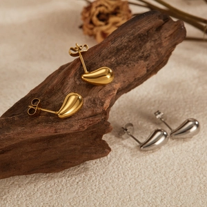 Detailed view of polished gold and silver water-drop stud earrings on rustic wood