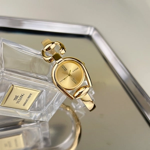 Macro shot of gold horsebit style bracelet watch with a sleek sunray dial on mirror surface