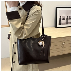 Detailed view of deep brown soft leather tote bag with baseball pendant charm on model