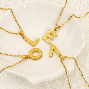 Golden titanium steel letter pendant necklaces on a white shell plate for men and women