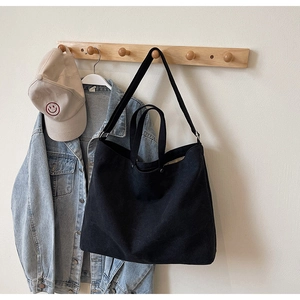 Large black canvas tote bag hanging with denim jacket and cap in a lifestyle setup