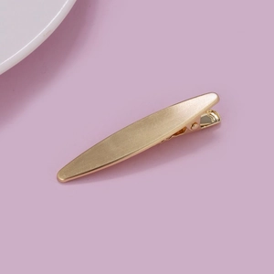 Minimalist golden metal spindle duckbill hair clip on a clean pink background