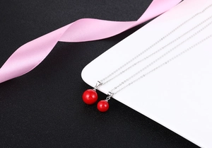 Detailed view of red pearl pendants with silver chains on a white plate with pink ribbon