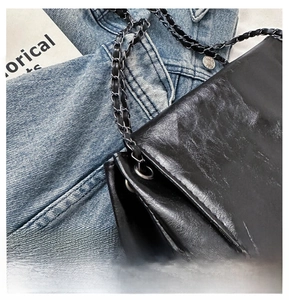 Detail of glossy pleated leather texture and intertwined metal chain strap on black bag
