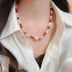 Close-up of irregular mother-of-pearl and red tube beads on a gold-tone necklace