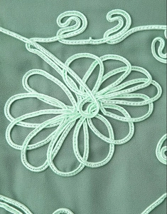 Detail of dark green fabric with light mint green rope embroidery in floral patterns